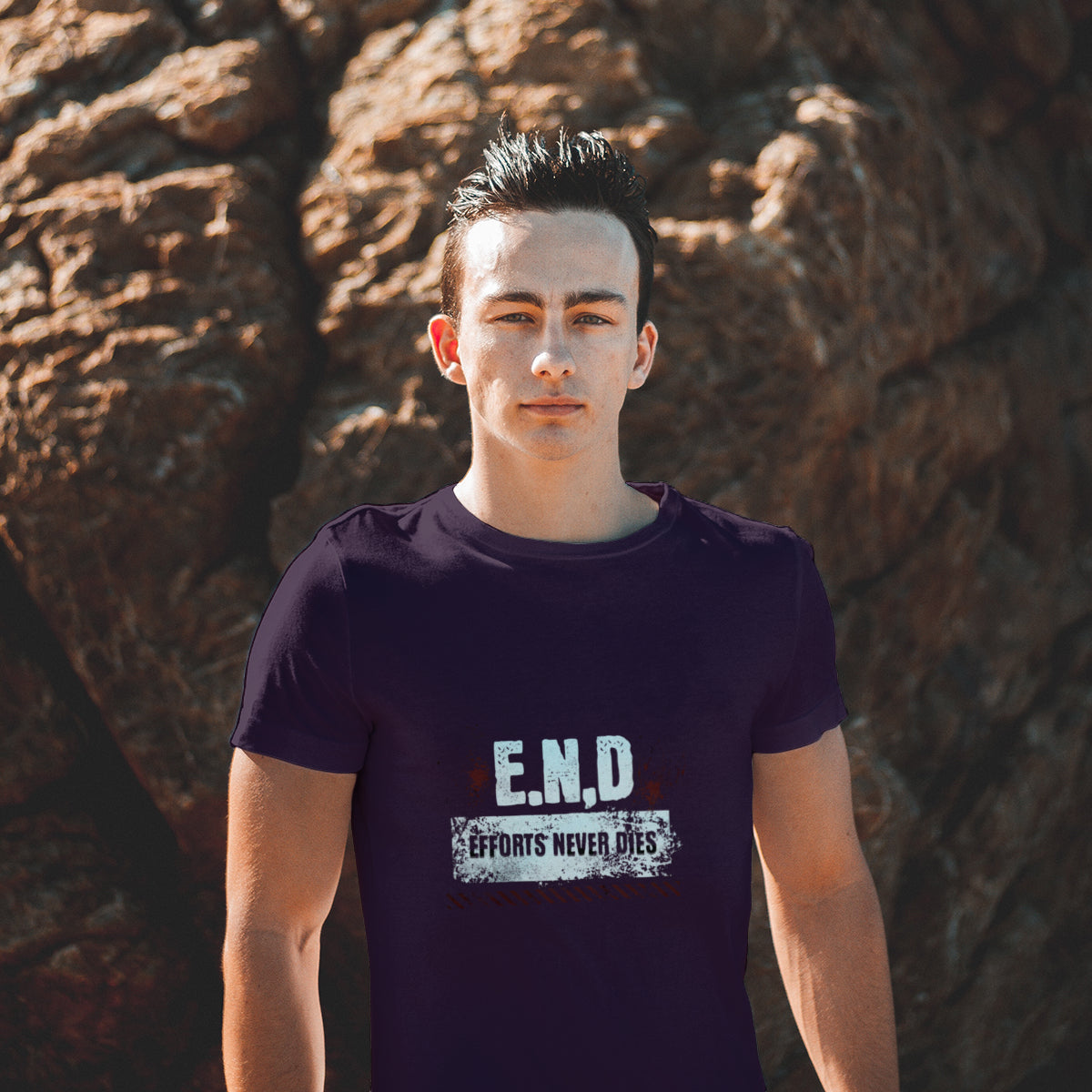 Person wearing a purple t-shirt with 'E.N.D. Efforts Never Die' text standing in front of a large rock.